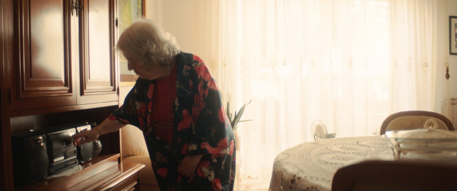 La Truffa, directed by Matteo Stipa and Michele Marchionne: Mirella, in a floral dressing gown, switches on the stereo in the living room cabinet