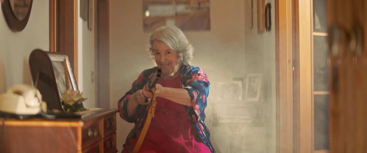 La Truffa, directed by Matteo Stipa and Michele Marchionne: Mirella in the hallway points a rifle, in the smoke of the shot