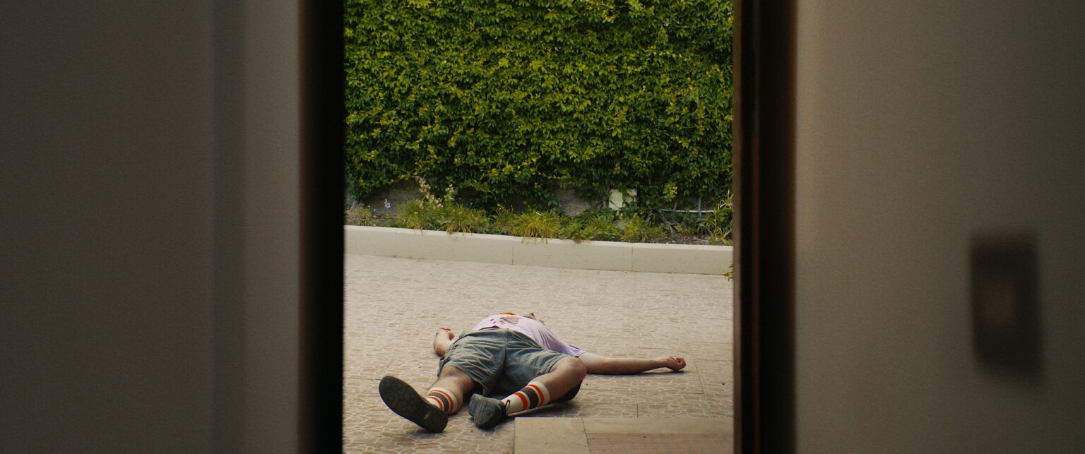 La Truffa, directed by Matteo Stipa and Michele Marchionne: a man lying in the paved courtyard, seen from the front door