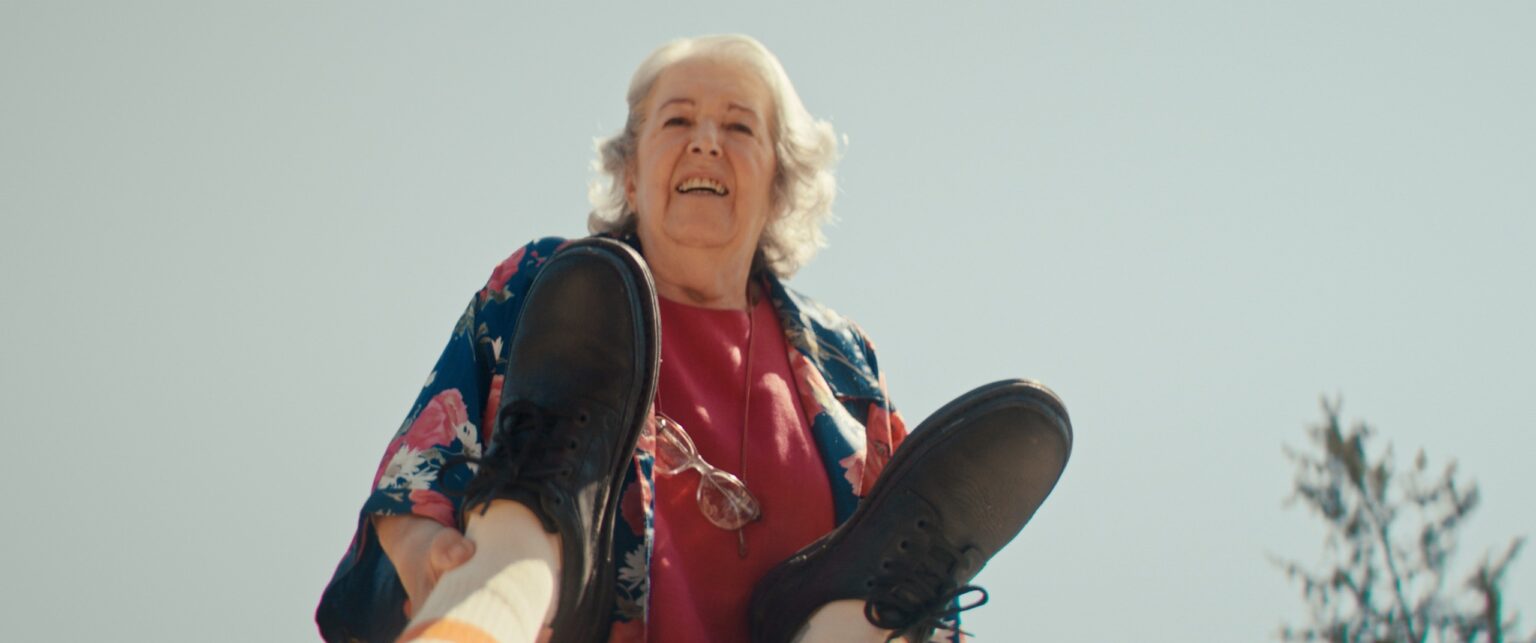 La Truffa, directed by Matteo Stipa and Michele Marchionne: Mirella laughs, seen from below against the sky, with two black shoes in the foreground